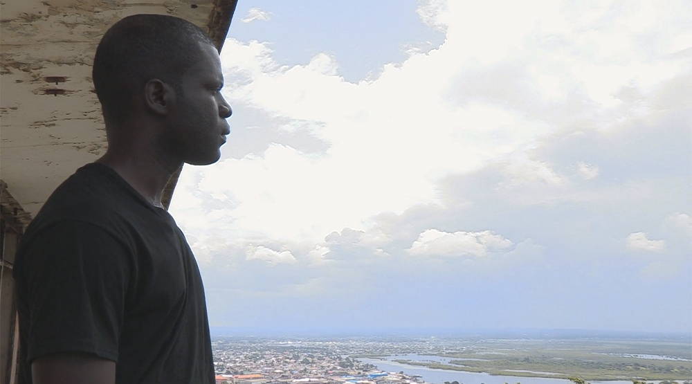 Emmanuel Urey standing over the ruins of the once-grand Ducor Hotel and looking over the slum community of West Point in Monrovia, Liberia. Photo by Sarita Siegel.