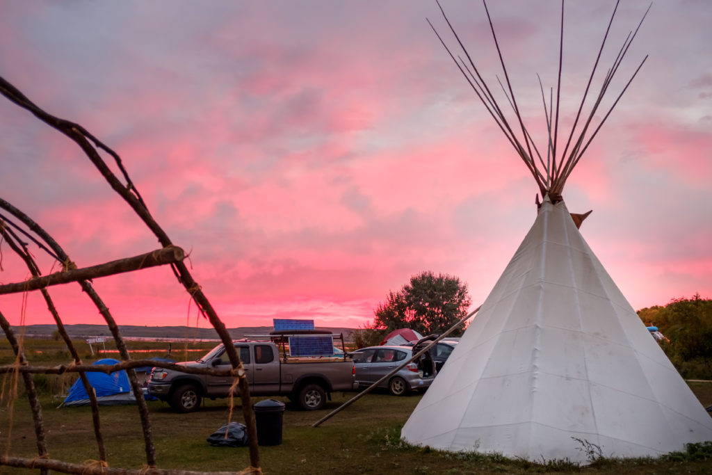 Dawn at the Sacred Stone camp. On the left is a longhouse frame. An Ojibwe supporter from Minnesota donated materials and his labor in order to construct several longhouses. This combination of teepees, nylon tents, tarps, and the longhouse is an example of the culturally and technologically eclectic nature of the camps. Image by author, September 2016.