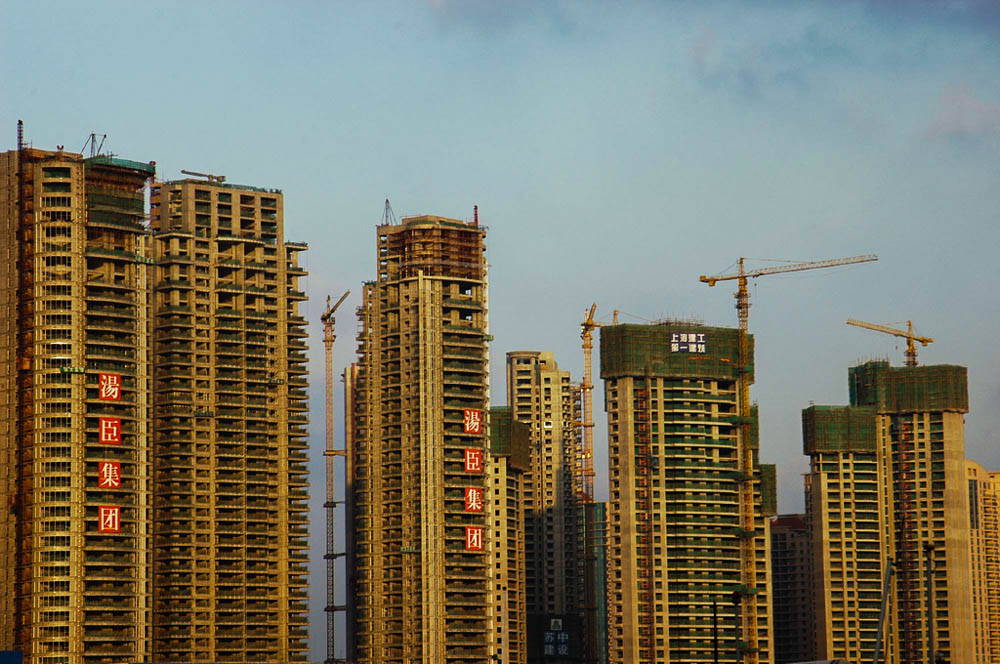 Four high-rise buildings against a skyline with cranes and Chinese characters.