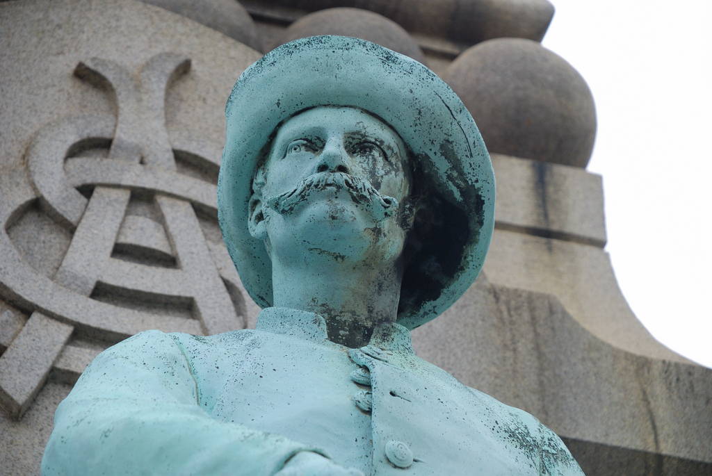 A bronze statue of a Confederate solider stands in front of a granite monument.