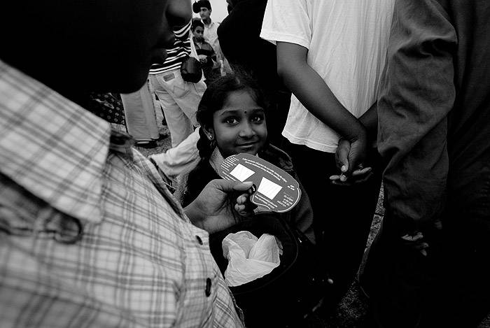 A girl in a crowd looks up at a man holding eclipse glasses and smiles