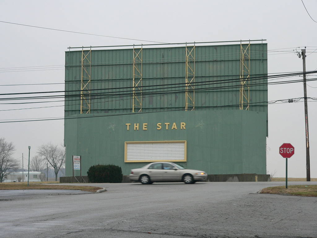 A blurry car drives past the backside of the abandoned drive-in movie theater, "The Star."