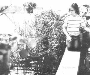 A child sits surrounded by plants in a greenhouse.