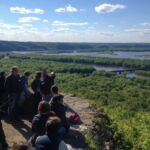 From bluffs overlooking the confluence of the Wisconsin and Mississippi Rivers at Wyalusing State Park, CHE community associate Eric Carson (associate professor in the Department of Environmental Sciences in UW-Extension, and a Quaternary geologist with the Wisconsin Geological and Natural History Survey) taught the group about fluvial geomorphology and introduced a major theme of the week: how in merging water and geology shape the changing flows of history. Photo by Elizabeth Hennessy. From bluffs overlooking the confluence of the Wisconsin and Mississippi Rivers at Wyalusing State Park, CHE community associate Eric Carson (associate professor in the Department of Environmental Sciences in UW-Extension, and a Quaternary geologist with the Wisconsin Geological and Natural History Survey) taught the group about fluvial geomorphology and introduced a major theme of the week: how in merging water and geology shape the changing flows of history. Photo by Elizabeth Hennessy.