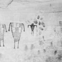 Countless petroglyph and pictograph panels dot the Bears Ears landscape. A black and white photograph of drawings of human figures and handprints on a cave wall.