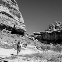 The author hiking up canyon. A black and white photograph of a man hiking through a canyon.