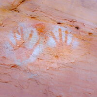 Handprints mark the presence of previous inhabitants from centuries before. A photograph of drawings of handprints on a stone wall.