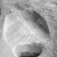 A depression has been worn in this sandstone boulder from grinding corn. Corn cobs and similar artifacts are common here. A black and white photograph of an indentation in the stone with an old corn cob inside.