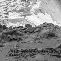 The roof of a kiva in an alcove. Kivas were likely used for ceremonies as well as for housing and storage. A black and white photograph of the remains of an ancient stone dwelling.