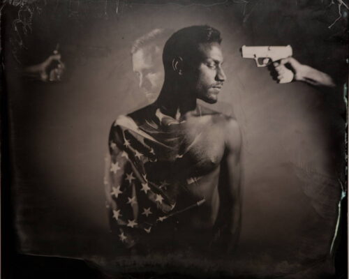 Eric Baillies. "American Life." Double-exposed tintype. 20x24. Original in private collection. In the foreground a dark-complected man stands shirtless. An American flag is draped over his left shoulder. In the mid-ground an arm reaches into the frame and points a gun at the man's face. In the background another man shadows the first along with another arm holding a gun.