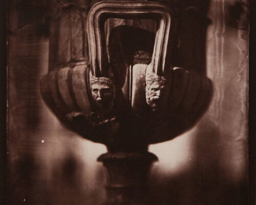 Eric Baillies. "Centennial Lamp Handle." Salt print. 8x10 The handle of a large urn fills the frame. At each end of the handle are two faces.