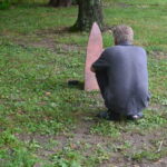 Public interaction with the installation. Image by Raina Martens, 2017. A man in a blue shirt crouches on the ground to look at a stone marker. Public Soil Memory exhibit.