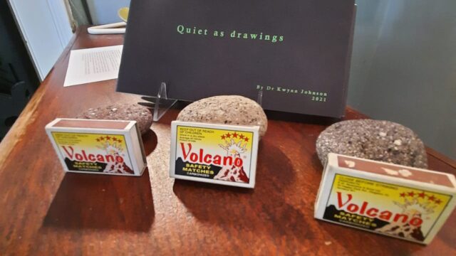 Volcanic material placed in Quiet as drawings exhibit. Photograph by David Cave, 2021. Rocks with volcano placard placed in glass box