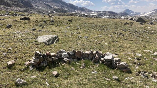 Portion of a stone wall. Photo by the author, 2021 Stones on grass, with some stacked to form a portion of a wall and mountains in the background