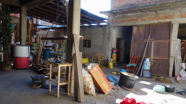 Household workshop, Teotitlán del Valle. In Oaxaca city, courtyards serve as leisure space or places for parking cars. In rural areas, families have room to spread out on surrounding grounds, and tend not to build courtyard homes. But in peri-urban areas, courtyards are often used as workshops for production of goods intended for urban markets. Since the grassland ecology on the mountain slopes around Teotitlán del Valle is good for pasturing sheep, residents produce high quality wool for knitting and weaving in their household workshops. A house's interior open air courtyard typical of Oaxaca's peri-urban landscape, serving as a workshop and storage and filled with supplies like buckets.
