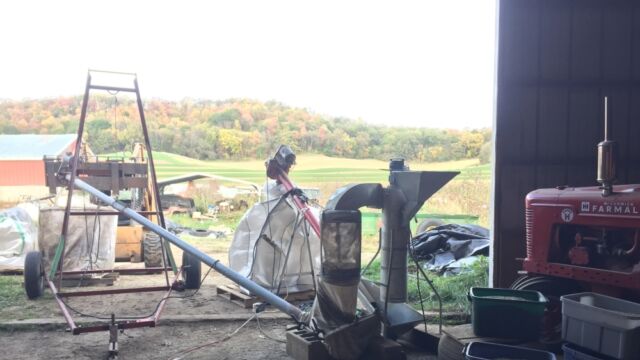 Cleaning the first harvest of Kernza from the Sauk County ARK project at the Gasser farmstead. Photo by the author, 2021. agricultural equipment in the doorway of a barn with a wooded hillside in the background